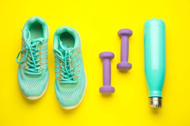 Dambıllar, ayakkabılar ve sarı arka planda bir şişe su.