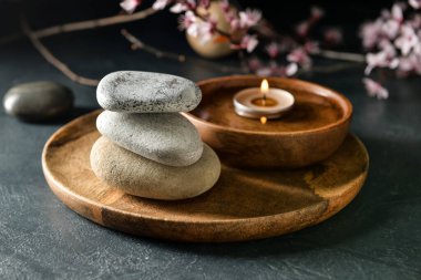 Koyu arkaplanda bir yığın kaplıca taşı olan ahşap tepsi