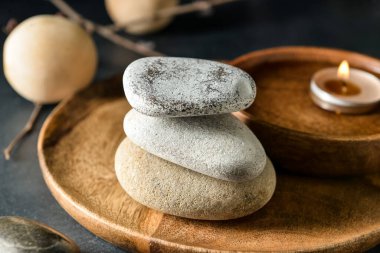 Koyu arkaplanda bir yığın kaplıca taşı olan ahşap tepsi