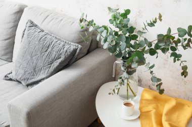 Okaliptüs dallı vazo ve oturma odasındaki masada bir fincan kahve.