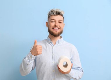 Tuvalet kâğıdı olan genç adam arka planda baş parmağını gösteriyor.