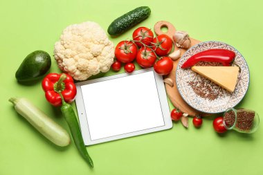 Boş ekranlı tablet bilgisayar ve yeşil arka planda sağlıklı yiyecek.
