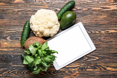 Boş ekranlı tablet bilgisayar ve koyu ahşap arka planda sağlıklı yiyecek.