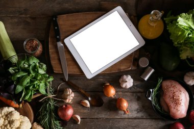 Tablet bilgisayar ve taze sebzeler mutfaktaki koyu ahşap masada.