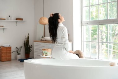 Evde banyo yaptıktan sonra bornozlu rahat genç bir kadın.