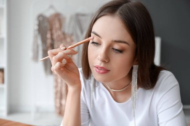 Güzel genç bir kadın soyunma odasında göz farı sürüyor, yakın plan.