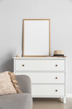 Işık duvarının yanında boş poster çerçevesi olan modern çekmeceler.