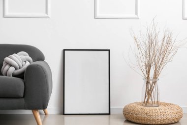 Boş poster çerçevesi ve cam vazodaki kuru dallar ışık duvarı yakınlarında.