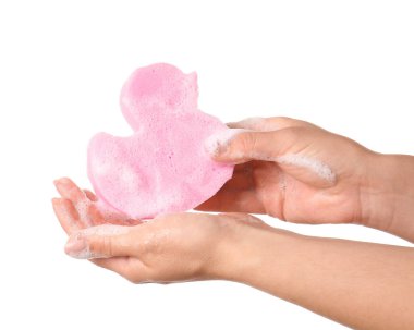 Beyaz arka planda sabunlu ördek şekilli banyo süngeri olan kadın elleri.