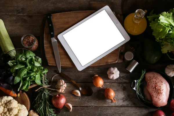 Tablet bilgisayar ve taze sebzeler mutfaktaki koyu ahşap masada.