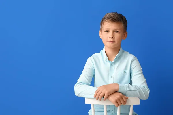 Kleiner Junge Sitzt Auf Stuhl Vor Blauem Hintergrund — Stockfoto