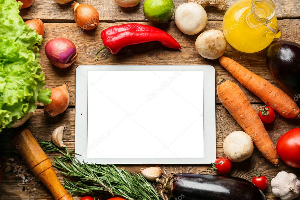 Tablet computer with tasty ingredients on wooden table