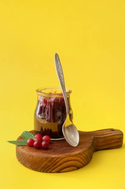Sarı arka planda kaşık ve bir kavanoz lezzetli kızılcık reçeli