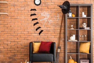 Cadılar Bayramı dekorasyonu tuğla duvarın yanında olan rahat bir koltuk ve raf.