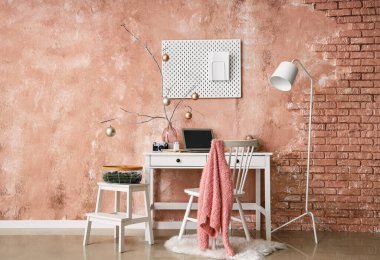 Vazoda Noel topları ve pembe duvarın yanındaki masada dizüstü bilgisayarlı ağaç dalları.