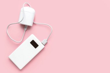 Modern güç bankası ve pembe arka plandaki kulaklıklar.