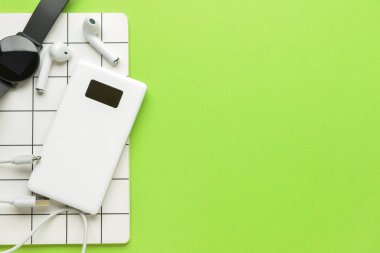 Modern güç bankası, kulaklıklar, not defteri ve yeşil arka planda akıllı arama.