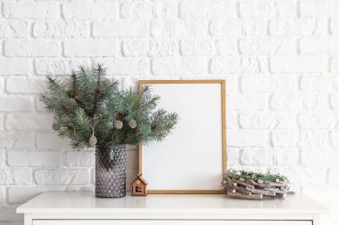 Köknar dallı vazo ve beyaz tuğla duvarın yanındaki rafta boş çerçeve