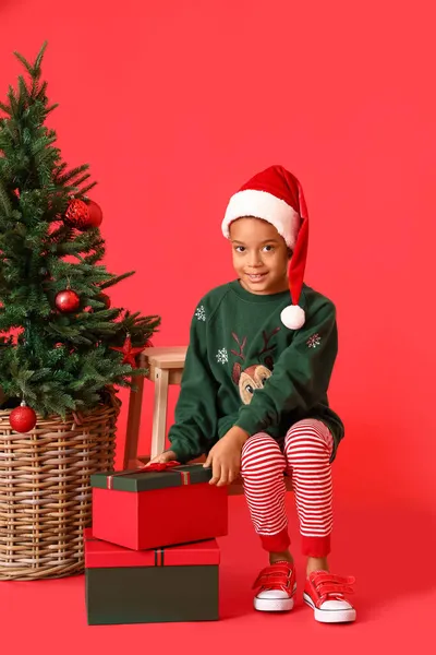 赤い背景にクリスマスの贈り物を持つ小さなアフリカ系アメリカ人の少年 — ストック写真