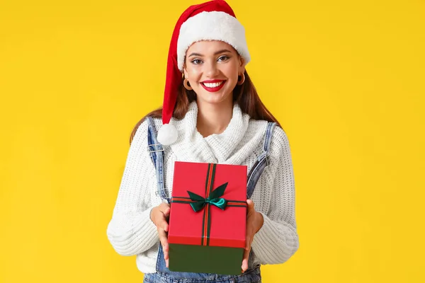 若いです女性でサンタ帽子クリスマスギフトとともに黄色の背景 — ストック写真
