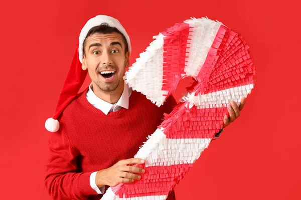 Überrascht Junger Mann Mit Weihnachtsmütze Mit Zuckerrohr Pinata Auf Rotem — Stockfoto