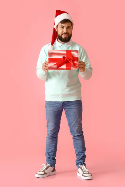 Schöner Mann Mit Weihnachtsmütze Mit Weihnachtsgeschenk Auf Rosa Hintergrund — Stockfoto