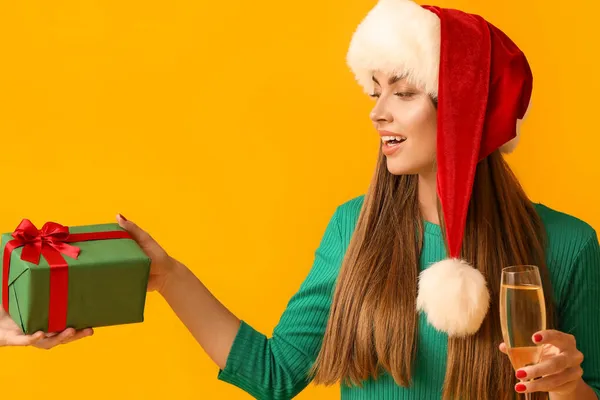 美しいです若いです女性でサンタ帽子受信クリスマスギフト上の黄色の背景 — ストック写真