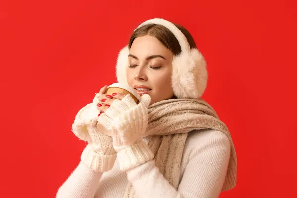 Schöne Junge Frau Warmen Ohrenschützern Trinkt Kaffee Auf Rotem Hintergrund — Stockfoto