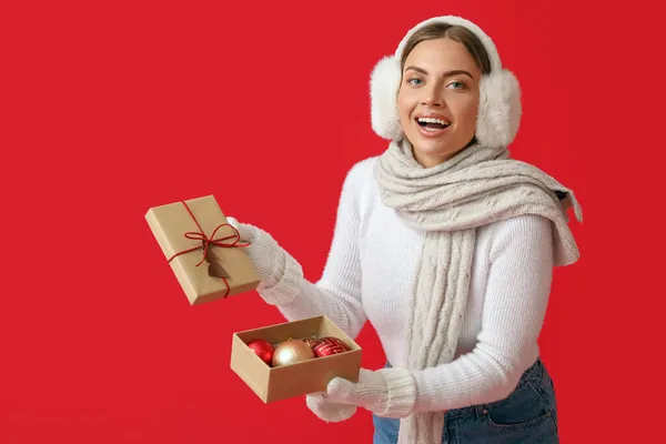 Schöne Junge Frau Warmen Ohrenschützern Öffnet Weihnachtsgeschenk Auf Rotem Hintergrund — Stockfoto