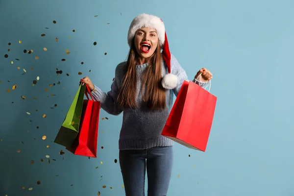 Happy Young Woman Santa Hat Shopping Bags Confetti Blue Background — Stock Photo, Image