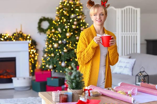 Beautiful Young Woman Drinking Hot Chocolate Wrapping Christmas Gift Home — Stock Photo, Image