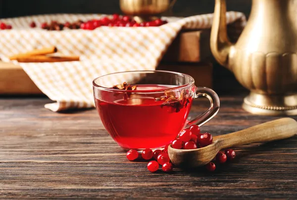 Cup of lingonberry tea and spoon with berries on wooden background