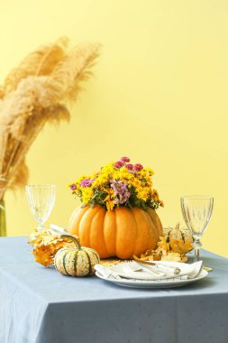 Bej duvarın yanındaki masada sunulan balkabağında güzel bir buket sonbahar çiçeği.