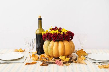 Beyaz duvarın yanındaki servis masasında sunulan balkabağında güzel bir buket sonbahar çiçeği.