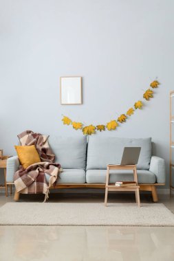 Rahat bir kanepe ve ahşap masa. Sonbahar yaprakları ve boş çerçeveli ışık duvarının yanında modern bir laptop var.