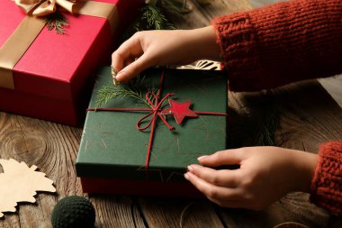 Noel hediye kutusunu tahta arka planda köknar dallarıyla süsleyen kadın.