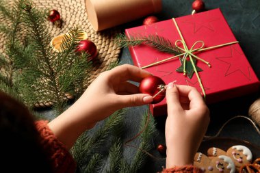 Siyah arka planda Noel topuyla hediye kutusu süsleyen kadın.