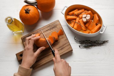 Beyaz ahşap arka planda balkabağı kesen kadın.