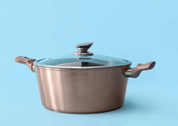 Stainless cooking pot with glass lid on color background