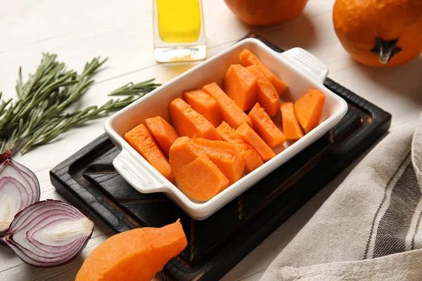 Beyaz ahşap zemin üzerinde balkabağı parçaları olan fırın tabağı