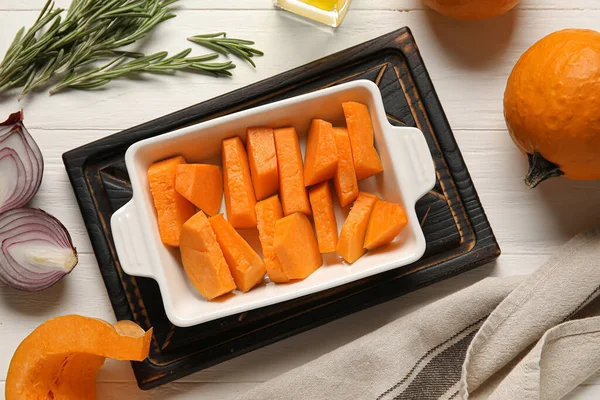 Beyaz ahşap zemin üzerinde balkabağı parçaları olan fırın tabağı