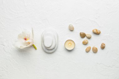 Çiçekli spa taşları ve beyaz arka planda yanan mum.