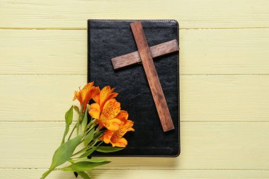 Sarı ahşap zemin üzerinde haç ve zambak çiçekleri olan kitap