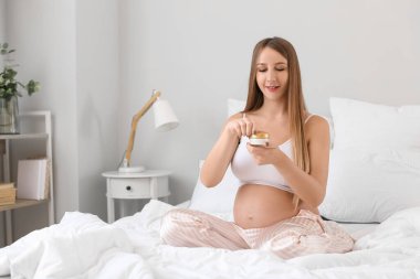 Yatak odasında bir kavanoz kremalı hamile kadın.