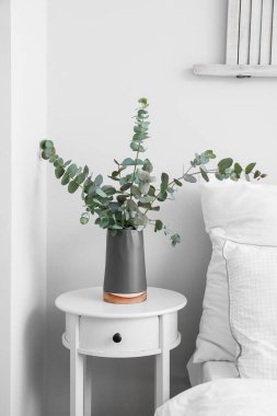 Okaliptüslü siyah vazo komodinin yanında, ışık duvarının yanında.