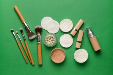 Yeşil arka planda farklı fırçalar, kozmetik ürünleri ve temiz pamuk pedleri