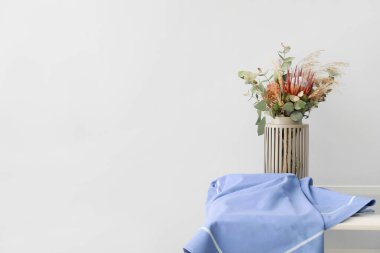 Beyaz duvarın yanındaki masada kurutulmuş çiçeklerle dolu bir vazo.