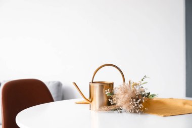 Su kovası ve kurutulmuş çiçek buketi beyaz masada, aydınlık odada.