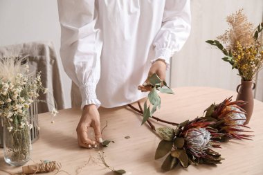 Kadın çiçekçi, masada kurutulmuş çiçeklerle buket yapıyor, yakın plan.