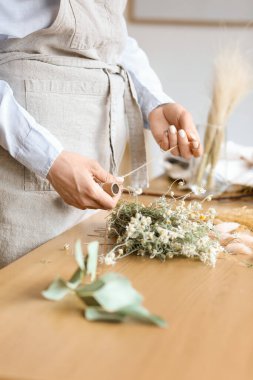 Kadın çiçekçi, güzel kurumuş çiçeklerle buket yapıyor, yakın plan.